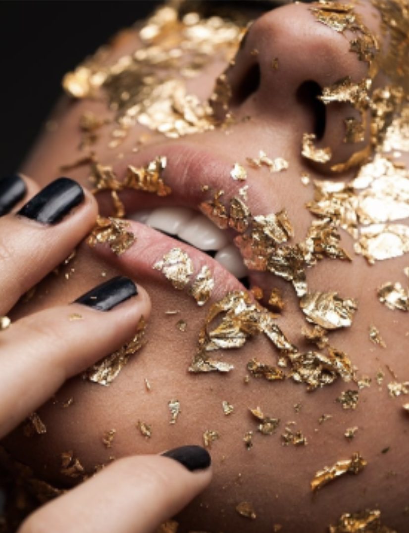 A woman with black nails and gold leaf on her body.